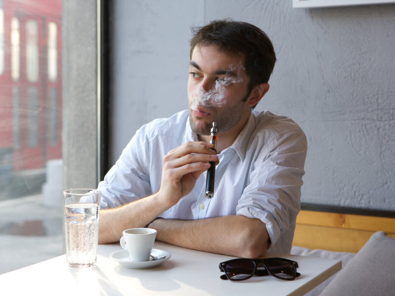 A man vapes an e-cigarette indoors at a restaurant