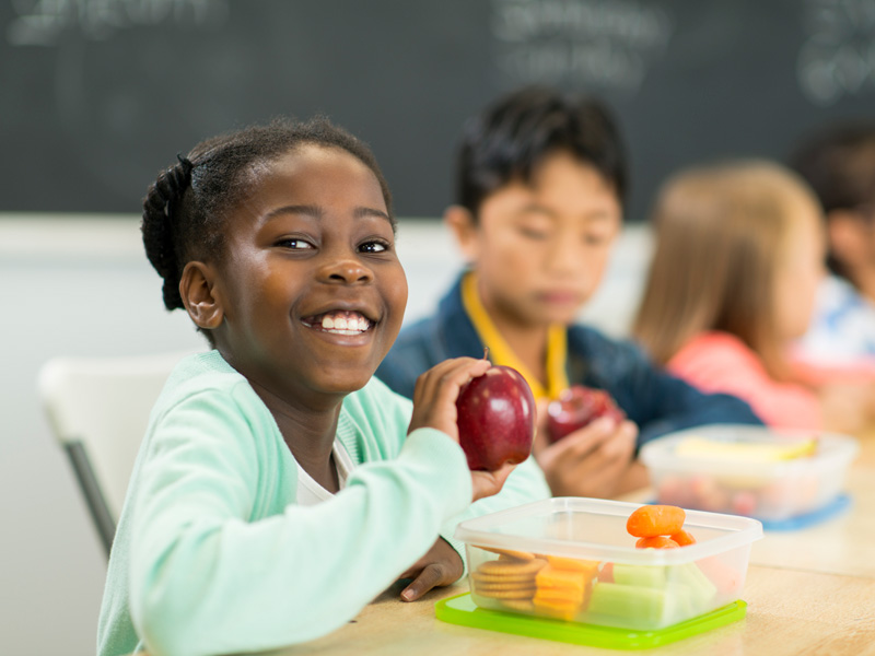 Students in a day care or elementary school cafeteria eat a variety of healthy foods