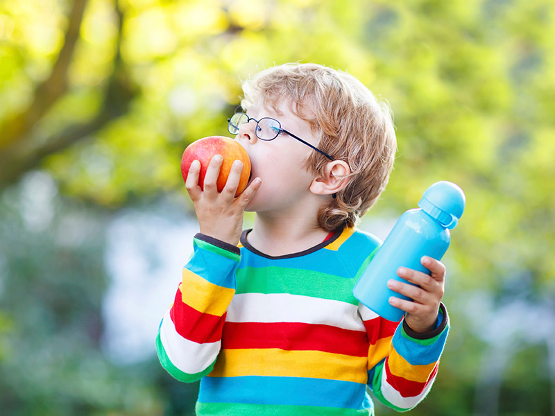 A young boy eats an apple and holds a water bottle
