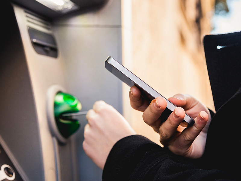 A bank customer uses an ATM and a mobile phone