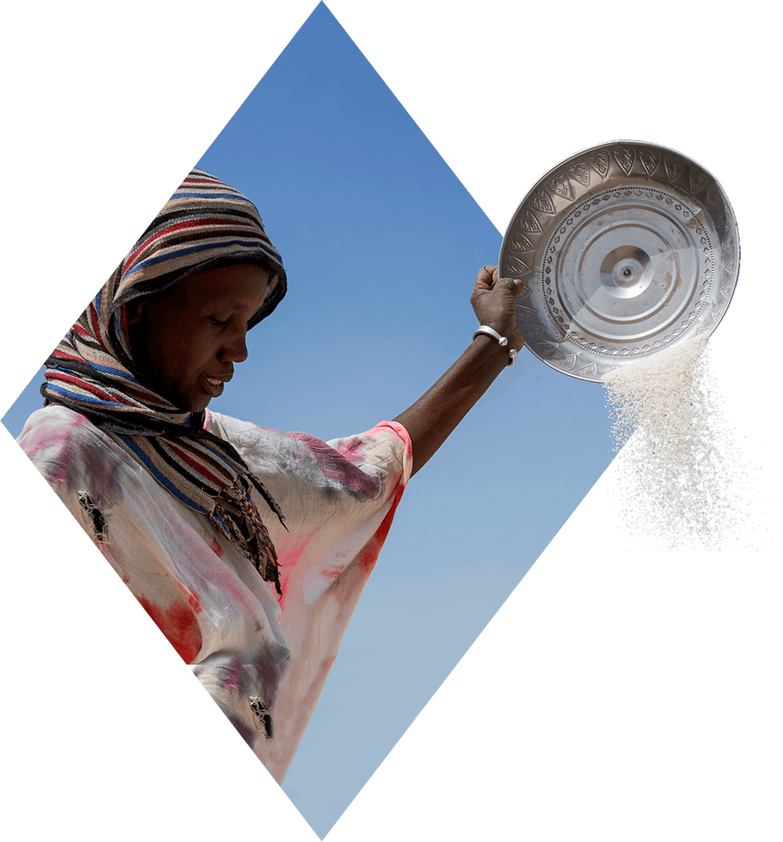 Woman in a headscarf sifting rice in a metal pan.