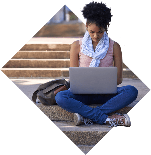 A student on her laptop, sitting crosslegged in front of some brick stairs with her backpack