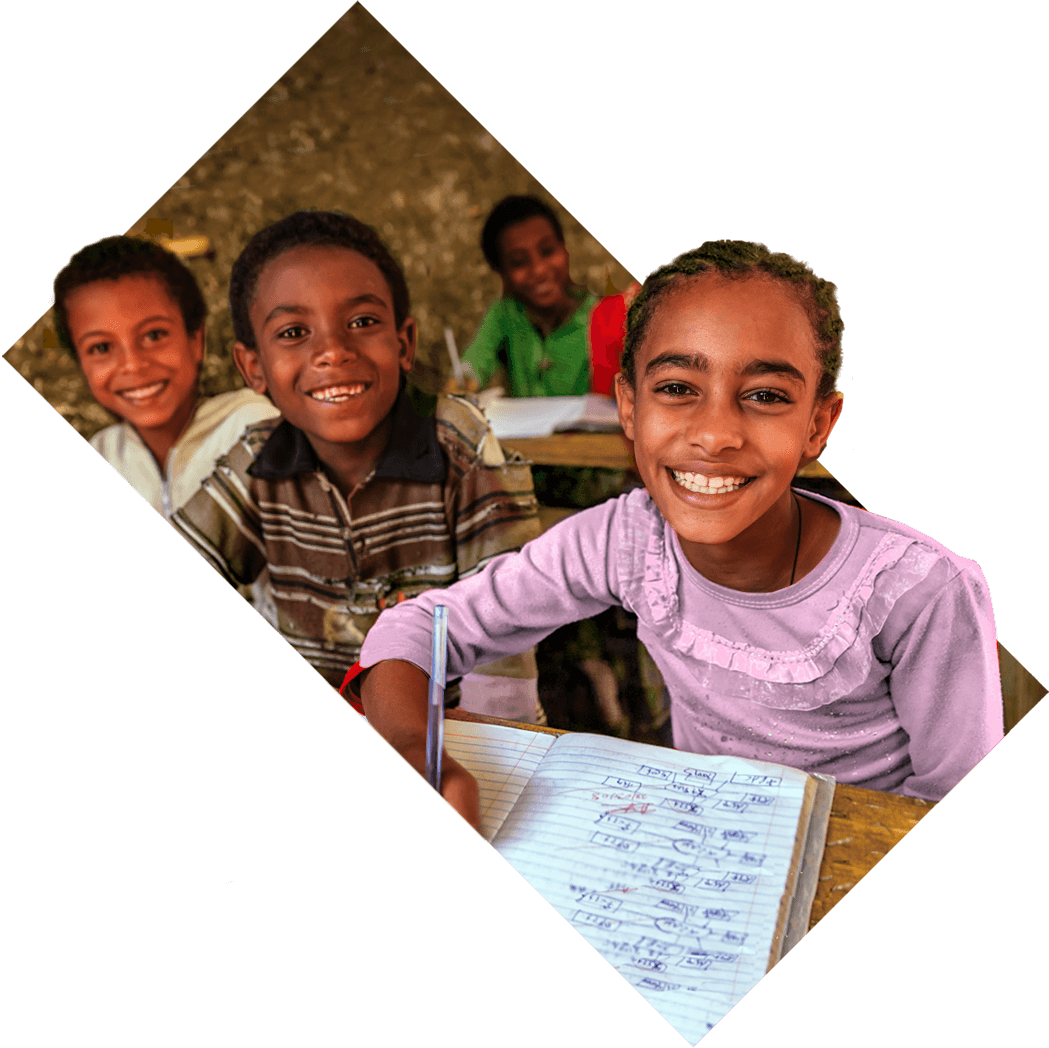 Smiling children seated in a classroom writing in notebooks.